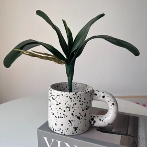 Close-up of realistic artificial orchid leaves displayed in a decorative speckled ceramic mug