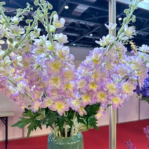 Primer plano de flores de delfinio artificiales moradas en un jarrón verde.