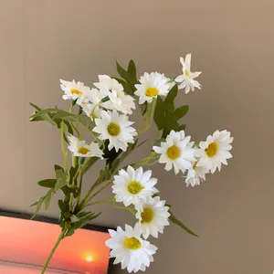 Detail view of lifelike white silk daisy flowers with textured yellow centers and green leaves