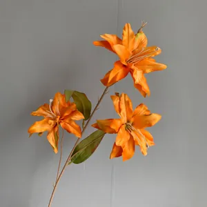 Detailed view of vibrant orange artificial lilies with green leaves on gray background.