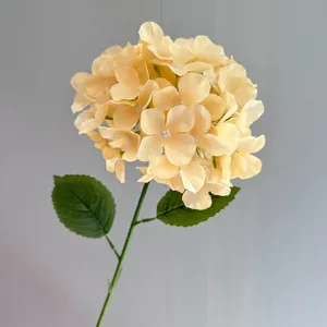 Detailed view of a cream yellow artificial hydrangea flower head with green leaves