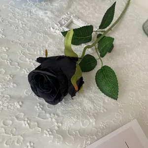 Close-up of a single black artificial Bulgarian rose on a white lace background.