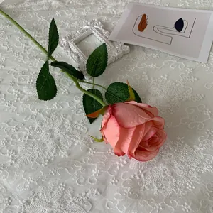 Close-up of a realistic pink artificial Bulgarian rose stem on a white lace background