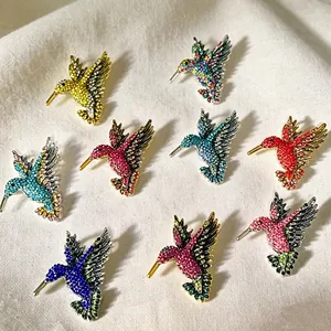 Collezione di spille colorate a forma di colibrì con strass su tessuto bianco