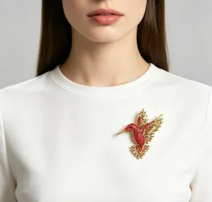 Dettaglio di una spilla a forma di colibrì con strass rossi su camicia bianca