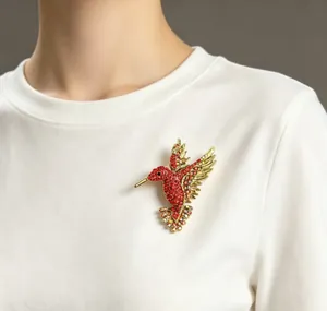 Dettaglio di un'elegante spilla a colibrì con strass colorati su una maglia bianca.