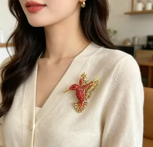 Dettaglio di un'elegante spilla a colibrì con strass rossi su un cardigan crema.