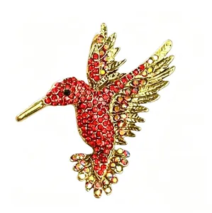 Vista macro dettagliata di una spilla a colibrì con strass rossi e base dorata.