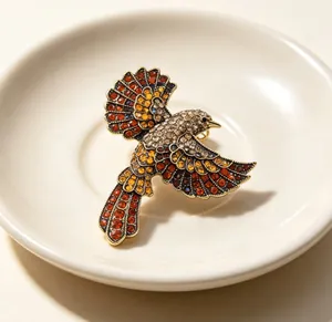 Nahaufnahme einer Vintage-Elsternbrosche mit orangen und klaren Strasssteinen auf Teller