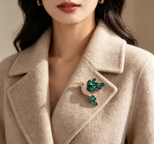 Detailed view of an elegant green crystal hummingbird brooch pinned to a beige wool coat