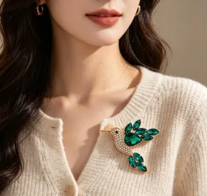 Detailed view of a gold bird brooch with green crystals on a cream cardigan.