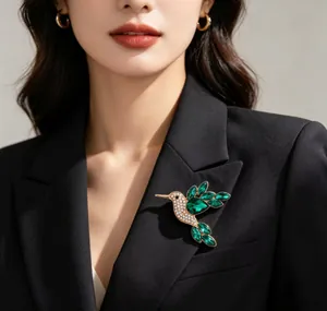 Macro detail of an emerald green rhinestone bird brooch pinned to a black lapel.