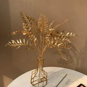 Gros plan d'élégantes feuilles de fougère artificielles dorées dans un vase moderne.