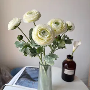 Detailed view of white artificial Ranunculus flowers in a glass vase on a table.