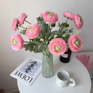 Detail of pink silk artificial ranunculus flowers arranged in a fluted glass vase.
