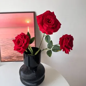 Close-up of realistic artificial red roses featuring delicate water droplets in a black vase