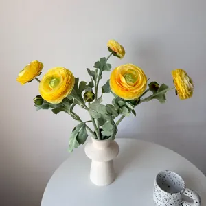 Detailed view of yellow artificial ranunculus flowers in a white ceramic vase.