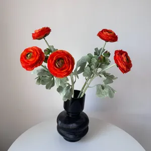 Vibrant orange artificial ranunculus flowers displayed in a black textured ceramic vase