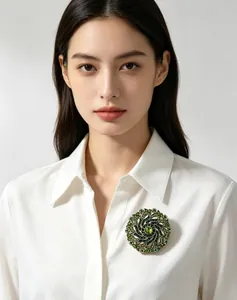 Close-up of an elegant green rhinestone swirling wreath brooch on a white shirt.