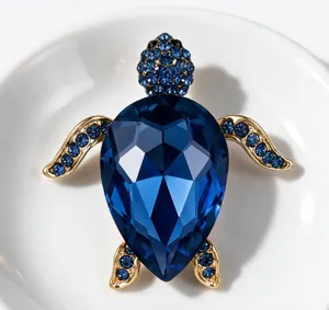 Gros plan d'une broche tortue de luxe dorée avec cristaux bleus facettés et strass.