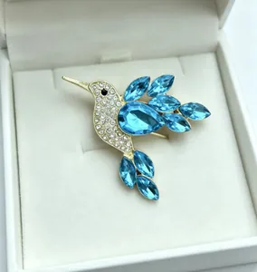 Close-up detail of a delicate hummingbird brooch with sparkling blue crystals in a white box