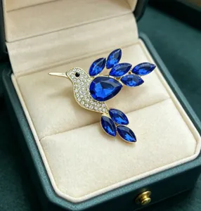Close-up of elegant gold hummingbird brooch with blue rhinestones in a green gift box.
