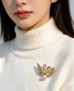 Vista detallada de un elegante broche de doble cisne con diamantes de imitación y perla.