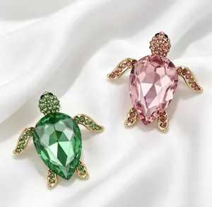 Détail de broches tortue de mer en cristal vert et rose sur fond de soie blanche