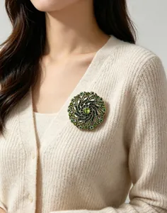Close-up detail of a vintage green rhinestone spiral floral brooch on a beige cardigan