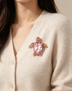 Gros plan d'une élégante broche tortue en cristal rose épinglée sur un cardigan en tricot
