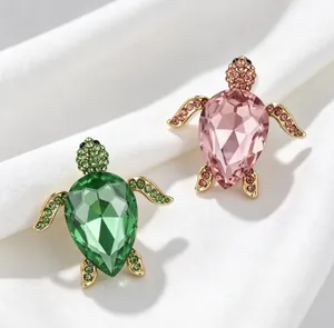 Gros plan détaillé de broches tortue en cristal vert et rose sur de la soie blanche.