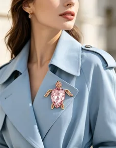 Gros plan d'une broche tortue en cristal rose étincelant sur un trench-coat bleu clair.