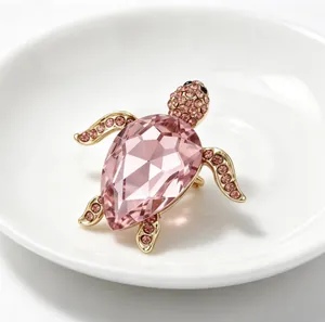 Gros plan sur la broche tortue en cristal rose avec métal doré et strass brillants.