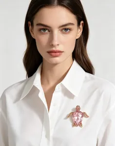 Détail d'une broche tortue en cristal rose à la mode épinglée sur une chemise blanche.