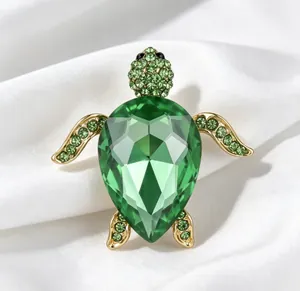 Détail d'une luxueuse broche tortue avec un grand cristal vert facetté sur la coque