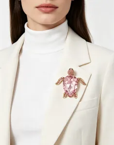 Détail d'une broche tortue en cristal rose épinglée sur un blazer blanc très élégant