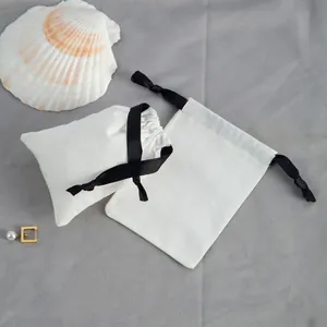 Détail de pochettes à bijoux en coton blanc cassé avec rubans noirs élégants.
