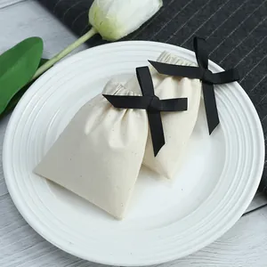 Détail macro montrant l'élégante pochette à bijoux en coton crème avec nœud noir.