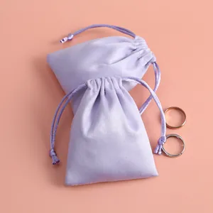Primer plano de bolsas de terciopelo lavanda con cordón para joyas sobre un fondo rosa
