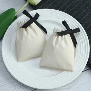 Gros plan de petits sacs en coton crème avec rubans noirs posés sur une assiette blanche