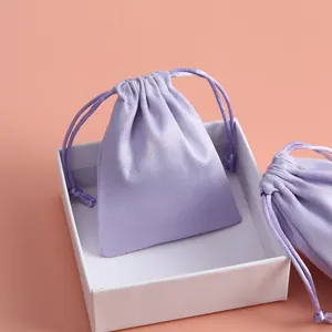 Vista detallada de una bolsa de terciopelo lavanda con cordón en una caja blanca