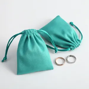 Bolsas de ante turquesa para joyas con cordón y anillos sobre un fondo blanco minimalista