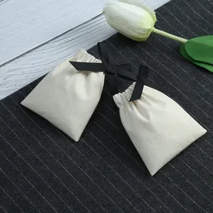 Gros plan de deux petits sacs cadeaux en coton beige avec des nœuds en ruban noir.