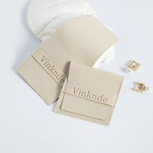 Detalle de bolsas de joyería de ante microfibra beige con logo y pendientes de perlas