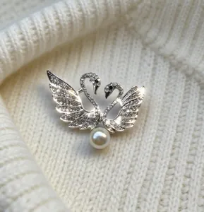Primer plano de elegante broche de doble cisne con cristales y perla sobre punto blanco