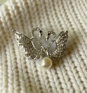 Primer plano detallado del elegante broche de doble cisne con diamantes y perla fina