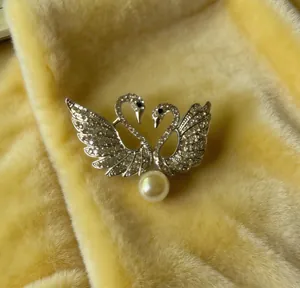 Primer plano de un broche de doble cisne con diamantes de imitación y una gran perla