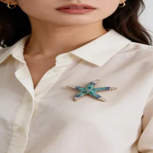 Detalle de un broche de estrella de mar vintage con cristales azules en camisa blanca.