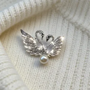 Exquisito broche de doble cisne con cristales y perla sobre fondo de suéter blanco de punto