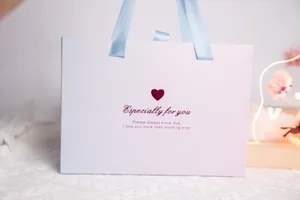 Détail d'un sac cadeau blanc avec des poignées en ruban bleu et un motif de cœur
